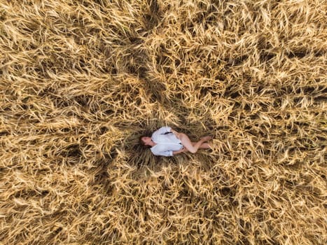 Aerial view of woman lying in the yellow field of wheat