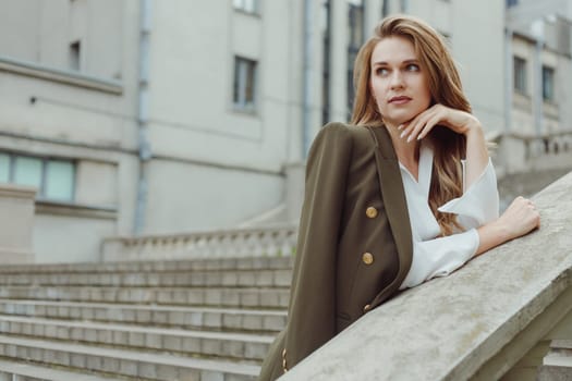 Fashionable woman in white pants and blouse with coat on shoulder posing outdoors. Women autumn look