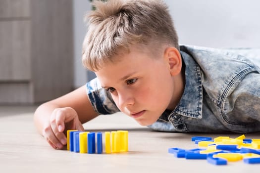 The boy neatly lines up colorful domino blocks on the floor of the home.