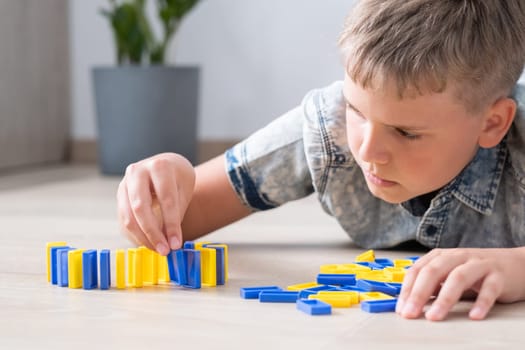 The boy neatly lines up colorful domino blocks on the floor of the home.