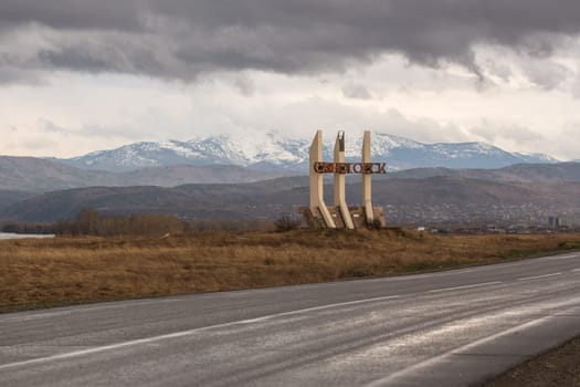 Sayanogorsk, Khakassia, Russia - a road sign-monument stella at the entrance to the city. Soviet vintage road decoration. Translation: Sayanogorsk.