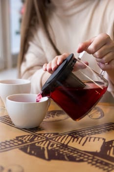 Pour the hot tea into a cup. The cup of tea on the wooden table was illuminated by the soft sunlight that penetrated the warm atmosphere