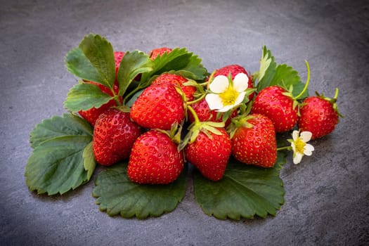 Red ripe strawberries with leaves over dark background