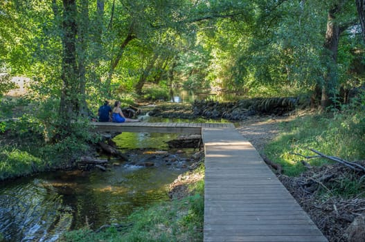 Gevora river, La Codosera, Badajoz, Extremadura, Spain. Mature couple sitting over wooden bridge