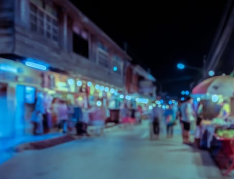 Blurred scene image of people walking at night market. Old wooden building town in Thailand