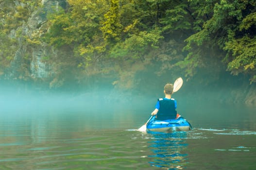 The young boy in  kayak in fog on mountain lake