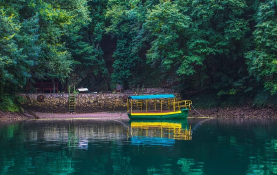 The old pleasure boat tied up near the shore against the background of a green forest
