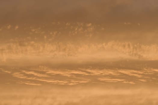 Sky and clouds in rich golden colours. Telephoto image of part of a sunset. Abstract cloud themed background with copy space. Warm evening feeling.