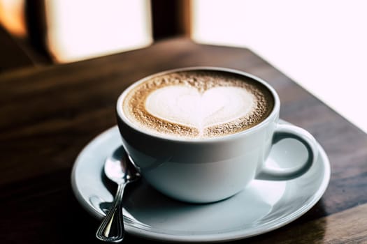 Cup of coffee latte with heart shape on old wooden background in the morning sunlight