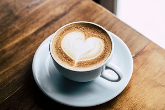Cup of coffee latte with heart shape on old wooden background in the morning sunlight