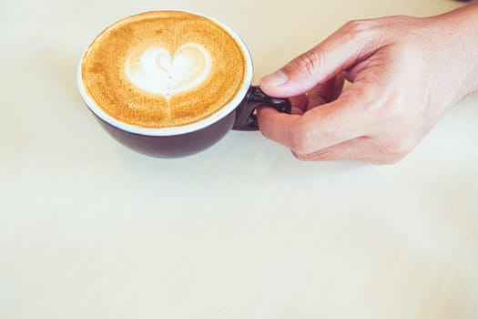 A hand take a cup of coffee latte with heart shape foam milk
