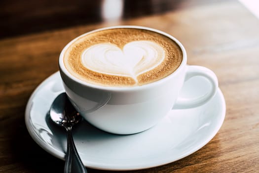 Cup of coffee latte with heart shape on old wooden background in the morning sunlight