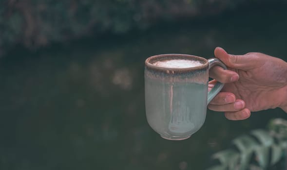 Hands of a man or barista holding cup of hot coffee latte with heart shaped foam art