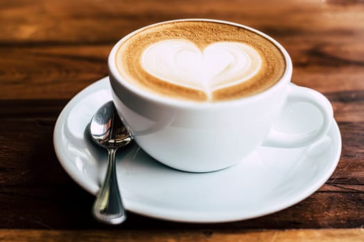 Cup of coffee latte with heart shape on old wooden background in the morning sunlight