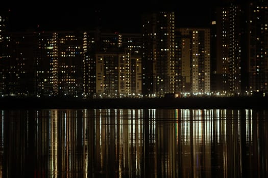 night light in the windows of skyscrapers is reflected in the river, cityscape