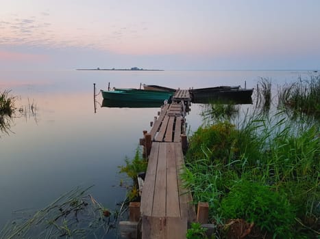 Quiet dawn in lilac and pink tones on the picturesque lake shore. Rowing boats are moored at a rural wooden pier. Russia, Rostov, Lake Nero. Space for copy.