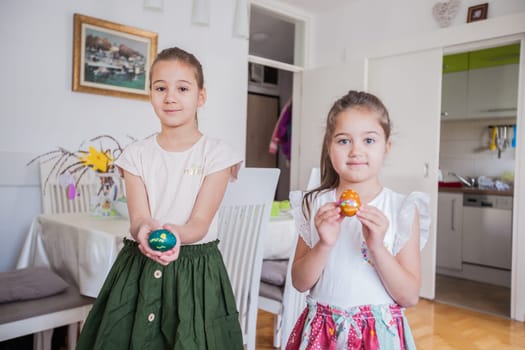 Portrait of two adorable little girls with colorful Easter eggs at home, Holiday day