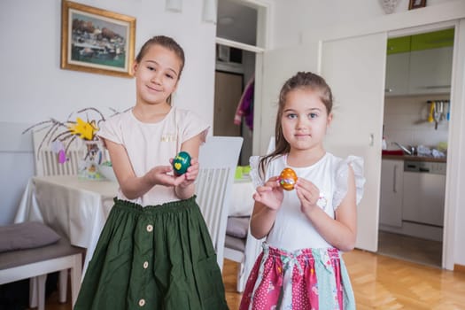 Portrait of two adorable little girls with colorful Easter eggs at home, Holiday day