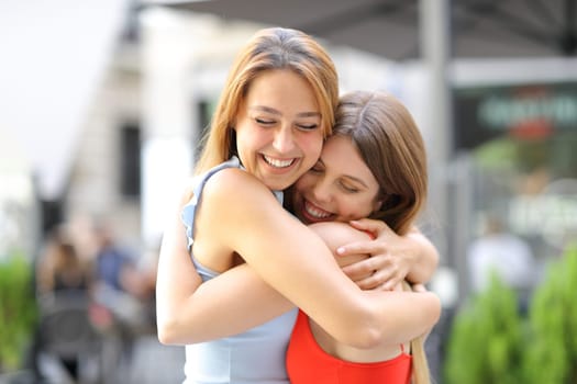 Happy friends hugging and laughing in the street on summer
