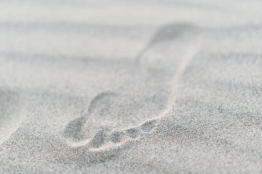 closeup top view of small child footstep imprinted in sand with shallow depth of field