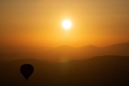 landscape with hot air balloon black silhouette rising up to the sky at sunrise with beautiful high mountain panorama in the background
