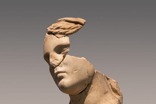 closeup portrait of antique damaged stone bust statue depicting a woman head with large pieces missing from the face area and large cracks in the marble