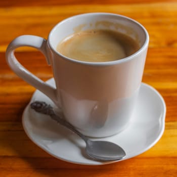 Black coffee crema in a white cup with spoon on a wooden table in Luang Prabang Laos.