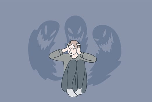 Phobias and inner fears concept. Young stressed man sitting touching head feeling bad with ghosts at wall from inside fears vector illustration