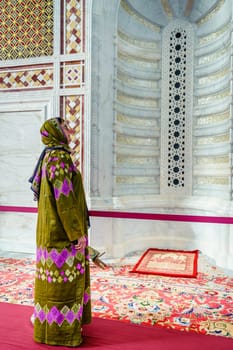 A woman dressed in a traditional omani abaya looking at an ornate alcove at the Muhammad al-Amin Mosque in Muscat, Oman