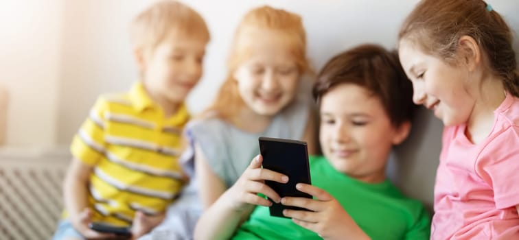 Group of children sitting indoors and looking in the smartphone. Concept of relationship, friendship and using of smart technologies.