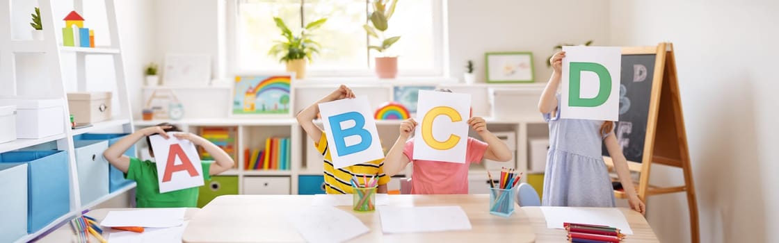 Children sitting in the classroom and showing the letters. Little kids learning an alphabet.
