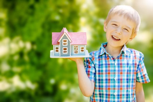Little child holding in his hand a model of the house. Concept of the family moving to another house, of the real estate, of the financial loan and mortgage.