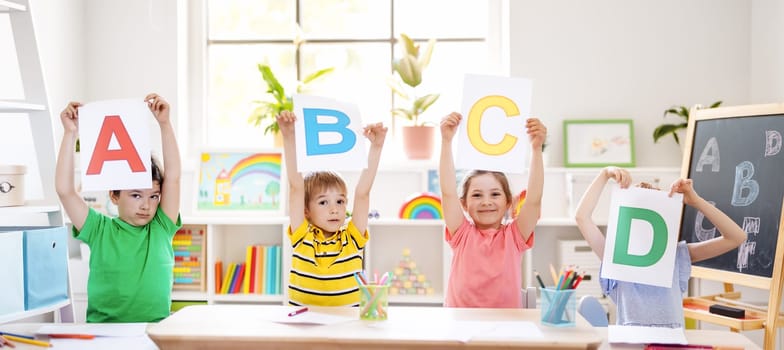 Children sitting in the classroom and showing the letters. Cute boys and girls learning an alphabet.