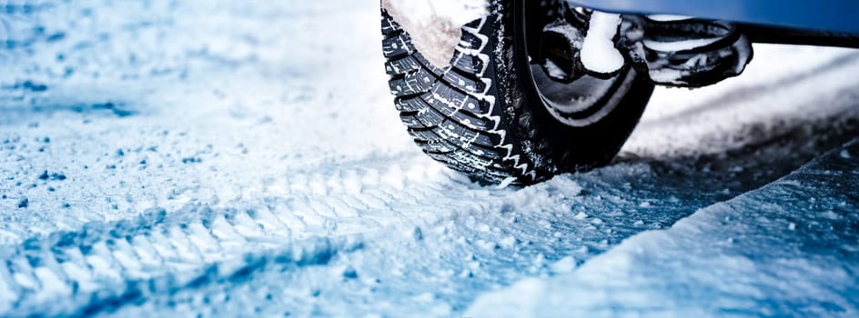 Car tires on winter road covered with snow. Panoramic view to vehicle on snowy way after snowfall