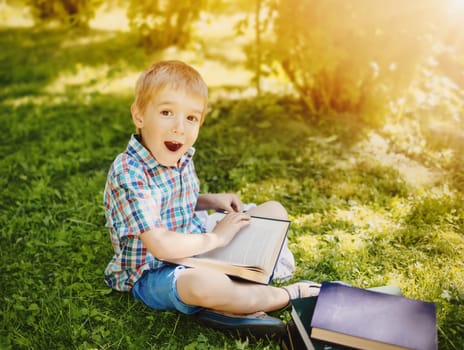 Little boy sitting on the meadow and reading a book. Concept of education and hobby.
