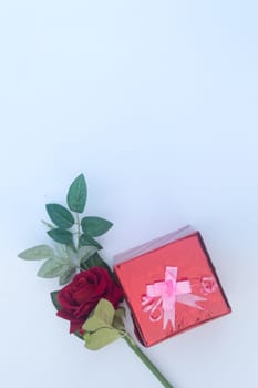 Gift box wrapped and tied with ribbon and a red rose in white background. Table top view. Flat Lay. Copy Space. Vertical.