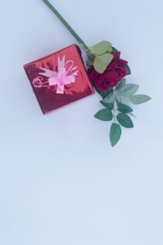 Gift box wrapped and tied with ribbon and a red rose in white background. Table top view. Vertical. Copy Space.