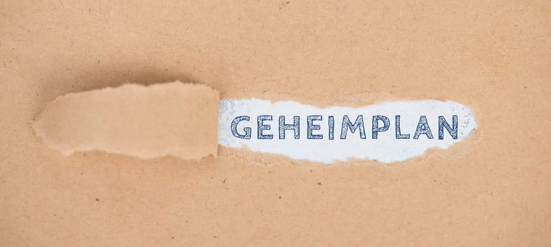 The german word secret plan is standing on a ripped paper
