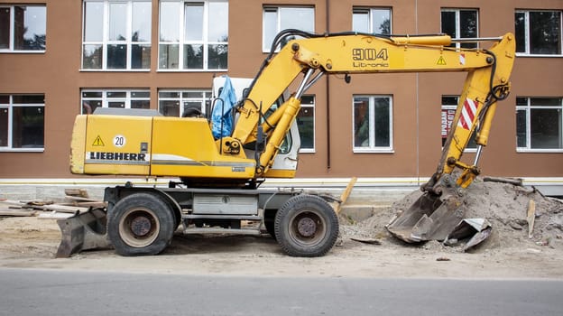 Mobile crane loader of yellow color on the background of a building under construction. International hardware manufacturer. The excavator is used for earthworks. Ukraine, Kiev - September 11, 2021
