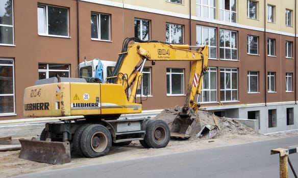 Mobile crane loader of yellow color on the background of a building under construction. International hardware manufacturer. The excavator is used for earthworks. Ukraine, Kiev - September 11, 2021