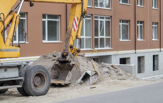 Mobile crane loader of yellow color on the background of a building under construction. German-Swiss international equipment manufacturer. The excavator is used for earthworks