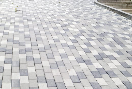 A long descent covered with gray paving slabs. The ramp is paved with concrete tiles. Wheelchair and bicycle accessibility concept