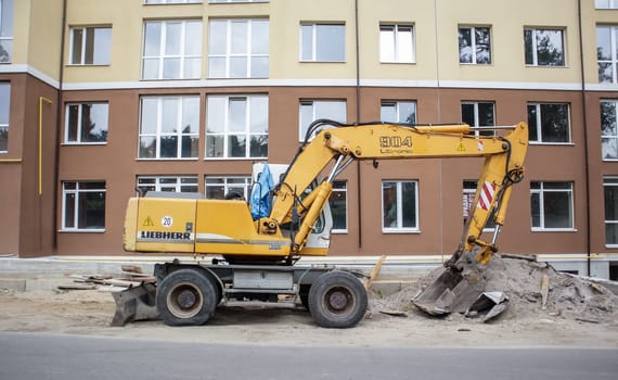 Mobile crane loader of yellow color on the background of a building under construction. International hardware manufacturer. The excavator is used for earthworks. Ukraine, Kiev - September 11, 2021