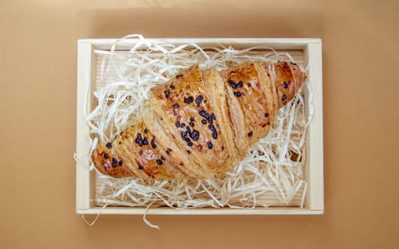 One regular fresh crispy whole grain croissant with chocolate filling on a brown or coffee background with copy space. Classic traditional freshly baked French dessert, pastries. Top view, flat lay