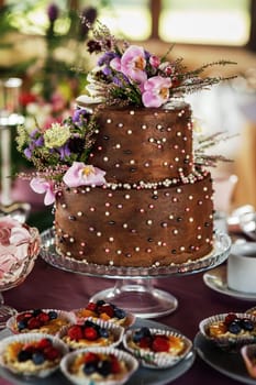 Two-tiered wedding cake beige. Decorated with handmade chocolate roses and artificial flowers. Photos in the interior. Hard light. Close-up.