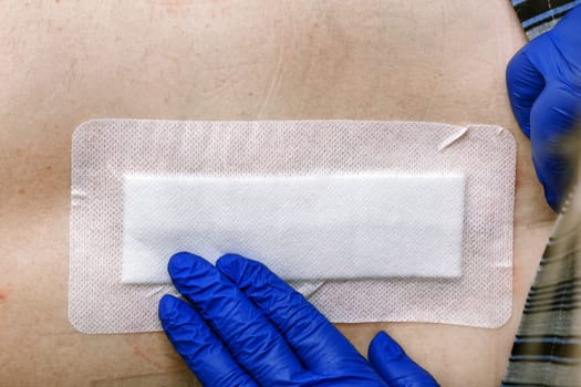 The nurse's hands are patching the postoperative seam with a plaster. Standard hospital dressing.