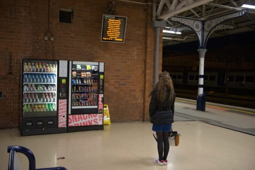 Doncaster, United Kingdom, 22nd May, 2021: Woman with long curly brunette hair and winter clothing contemplates which vending machine to purchase from