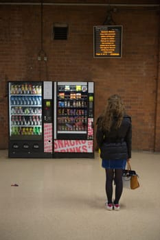 Doncaster, United Kingdom, 22nd May, 2021: Departure board displays COVID information for rail travel, read by a young woman stood by vending machines