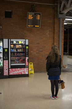 Doncaster, United Kingdom, 22nd May, 2021: Vertical image of a winter clothed young woman reading doncaster train station departure board. Late night