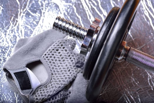 Fitness equipment dumbbell weights and fitness gloves on a metallic background
